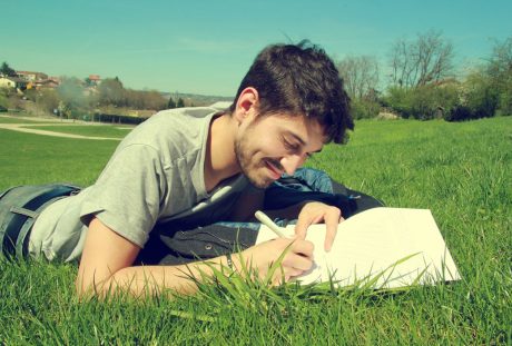 趴在草地上记录写字的男子图片